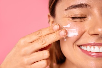 caucasian woman with clear glowing skin using facial moisturizer or sunscreen isolated on pink background. facial skin care. spa treatments and cosmetology.
