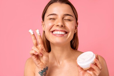 caucasian woman with clear glowing skin using facial moisturizer or sunscreen isolated on pink background. facial skin care. spa treatments and cosmetology.