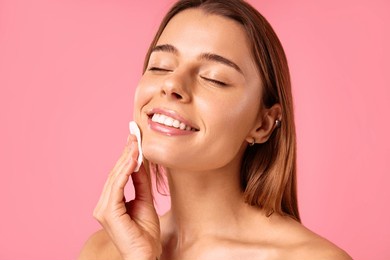 caucasian woman with clean glowing skin using cotton pads wiping face with toner or removing makeup isolated on pink background. facial skin care. spa treatments and cosmetology.