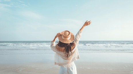 summer beach vacation concept, happy young woman with hat relaxing with her arms raised to her head enjoying looking view of beach ocean on hot summer day, copy space