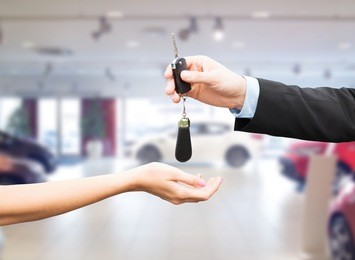 auto business, car sale, transportation, people and ownership concept - close up of car salesman giving key to new owner or customer over auto show background