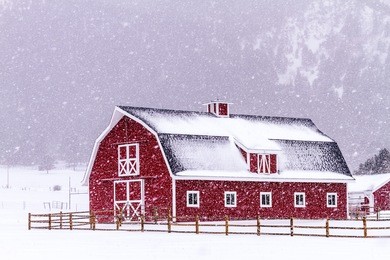 bright red barn covered with snow surrounded with wooden fence on snowy winter day