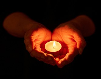 hands, dark and person with candle, light and offering with religion on studio background. closeup, model or human with open palms, solidarity or night with support, spiritual or ritual for vigil