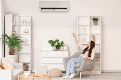 beautiful woman in armchair switching on air conditioner at home