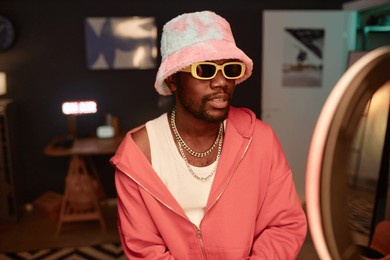 waist up portrait of trendy black young man wearing pink outfit and recording videos for social media with ring light