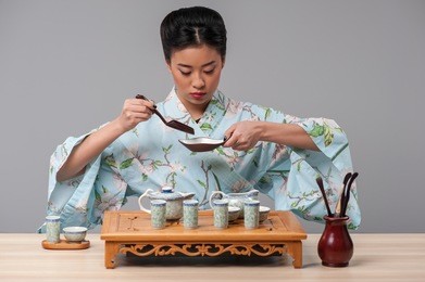 asian culture. young beautiful japanese woman in traditional kimono getting ready to perform tea ceremony with tea tools on the table against grey background 