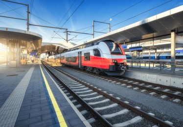 high-speed red passenger train at railway station platform under clear blue sky at sunset. train station. modern railway transportation concept. railroad. commercial. urban rail transport in austria