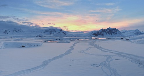 amazing sunset over snowy antarctic landscape. snow covered frozen polar ocean and mountain range under colorful sunrise sky. arctic winter nature. antarctica travel and exploration. aerial drone shot