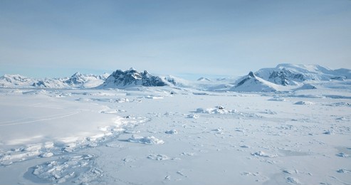 cold south pole winter landscape in sunny day. snow covered frozen polar ocean, mountain range in background. antarctica aerial majestic seascape drone view. beauty of wild untouched nature. travel