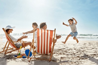 family, children and playing at beach chair, vacation adventure and jump with bonding on summer journey. parents, kids and excited for ocean freedom, energy and sunshine travel in bali island