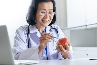 cardiologist supports the heart senior asian woman doctor wearing glasses and uniform. portrait of mature old asian woman medic professional.