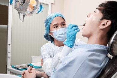 asian female dentist examine young male patient teeth and toothache stomatology in dental clinic, well-being hygiene checks, and professional orthodontic healthcare work in doctor's office hospital.