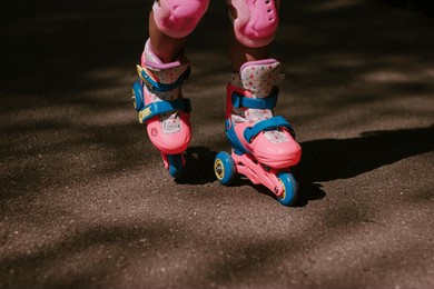 a little girl in knee pads learns to ride pink roller skates outside in summer in hot weather. video training. roller skating in the park. summer holidays. protection of elbows and knees from falling