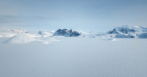 fly over snow covered arctic winter landscape, towering mountains in background. aerial view of frozen antarctica panorama under blue sky in sunny day. polar frozen ocean. low angle aerial drone shot
