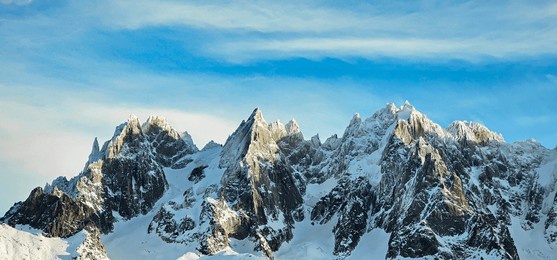 looking up at three craggy, rocky peaks in the french alps above ski resort town of chamonix, by mont blanc, with snow on mountain tops, blue sky and sunlight on the rocks and snow
