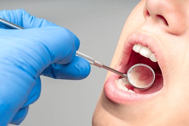 close up of dentist hand examining patient teeth with dental mirror.