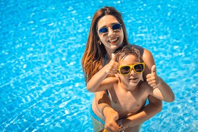 happy mother and boy gesturing with thumbs up inside a blue pool water