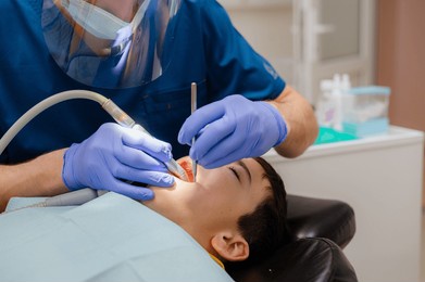 cute little boy is sitting in a dental chair with a scared expression on his face, afraid to treat his teeth. prevention of diseases of baby teeth in children.