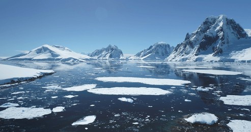 antarctica ocean bay aerial landscape in sunny day. melting ice floe on water surface, blue sky, snow covered mountains in background. antarctic travel exploration. discover beauty of south pole