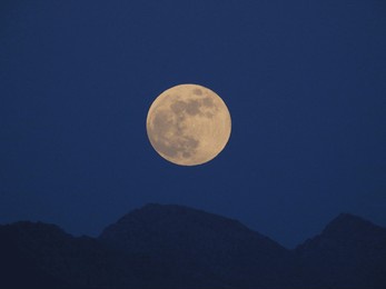 a big, bright full moon shines in the evening sky above dark mountain peaks