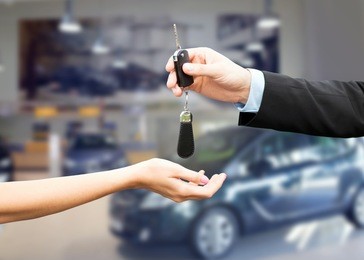auto business, car sale, transportation, people and ownership concept - close up of car salesman giving key to new owner or customer over auto show background