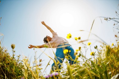 summer mood. a young and cheerful guy dances against a background of blue sky and flowers. a handsome man dances among flowers. happy young guy among blooming flowers, outdoors. spring fashion.