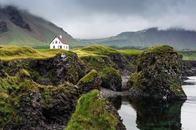 sea shore with cliffs and small white house on a cloudy day, arnarstapi, west iceland
