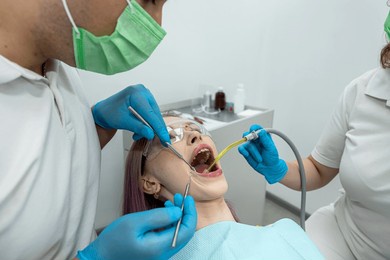 smiling dentist and an assistant talk to a patient while checking her teeth during a dental procedure in the dentist's office. dentistry teeth