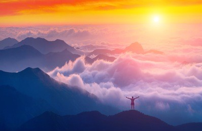 man standing on a mountain top with raised hands and welcome sunrise in a crimea mountains above the cloudy valley