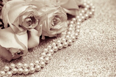 pink rose and pearl necklace on a shiny gold background
