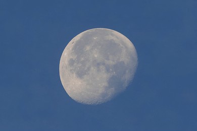 full moon seen with astronomic telescope over blue sky in the morning