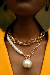 chicago, il 05-24-24: a close-up of a person's neck adorned with stylish gold and pearl necklaces, complemented by large geometric earrings and a vibrant yellow outfit.
