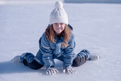 happy girl, child sitting on ice in winter in skates smiling . high quality photo