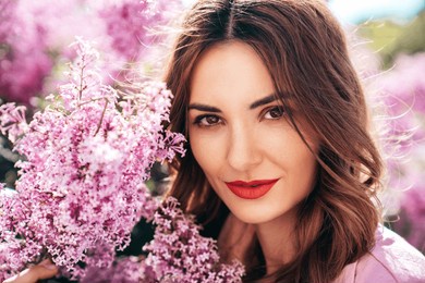 young beautiful smiling woman. sexy carefree model posing in the street. positive model near blooming flower lilac bush beaming. summertime, pink colours. closeup beauty portrait, red lips