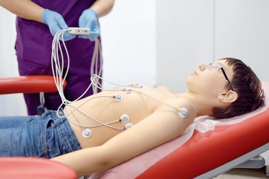 child under ecg test with doctor. boy patient lying in medical bed with vacuum sensors. a nurse performs an electrocardiogram of the heart in office of a medical clinic. checkup of heart