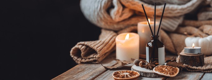 home comfort, coziness, aromatherapy. cozy interior with knitting, burning candles and aroma perfume diffuser in the living room. fall scent, sweet pumpkin pie fragrance dry leaves, autumn mood banner
