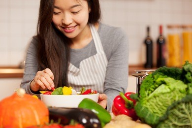 photo of asian young woman composing a colorful salad at home in the kitchen