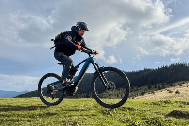 cyclist man riding electric mountain bike outdoors. male tourist biking along grassy trail in the mountains, wearing helmet and backpack. concept of sport, active leisure and nature.