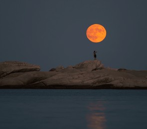 august full moon at the beach with rocks and a girl 