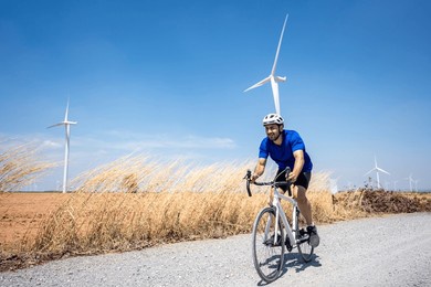 caucasian active sportsman riding bicycle at the wind turbine field. attractive athlete in sportswear exercise by cycling workout outdoors for health and wellness in rural area at windmill power farm.