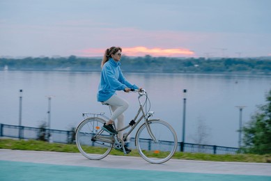 woman rides a bicycle along a riverside path during sunset, enjoying a peaceful evening outdoors by the water.evening cycling before going to bed, an active lifestyle