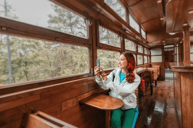 tourist woman using a smartphone to take selfie photo in the retro train wooden carriage interior