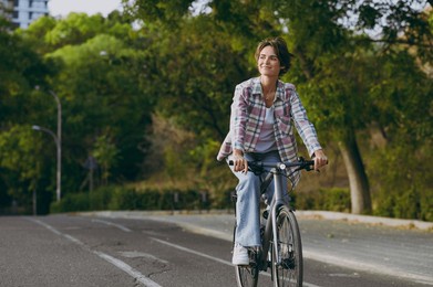 full body young happy fun smiling woman wearing checkered shirt casual clothes look aside walk riding bicycle rest relax in spring sunshine green city park outdoors on nature. urban leisure concept