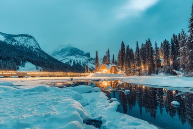 beautiful winter scene of wooden lodge glowing on emerald lake and pine forest at yoho national park, british columbia, canada
