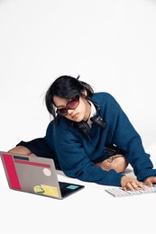 young asian female office worker, full body fashion photoshoot in studio, isolated on white background, the concept of office syndrome, working on a laptop or computer, wearing sunglasses, blue shirt