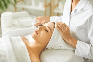 close up beautician's hands applying anti-aging facial cream on woman client face to prevent wrinkles in spa salon. skin care, cosmetic procedures for facial care and beauty treatment concept.