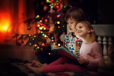 children reading an interest book sitting on the bed against the decorated christmas tree