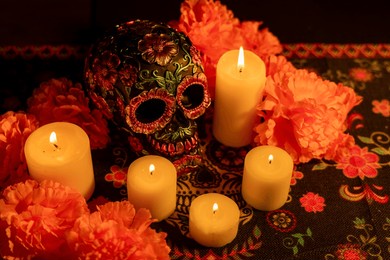 a detailed skull decorated with metallic flowers and surrounded by vibrant marigolds. five candles illuminate the scene, with all elements placed on a day of the dead-themed tablecloth