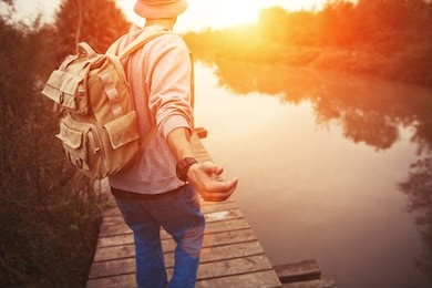 traveler with backpack walking over wooden bridge on the lake in sunset