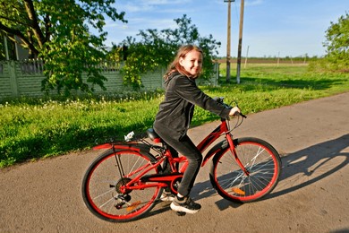 a child girl rides a bicycle in the spring in the village.